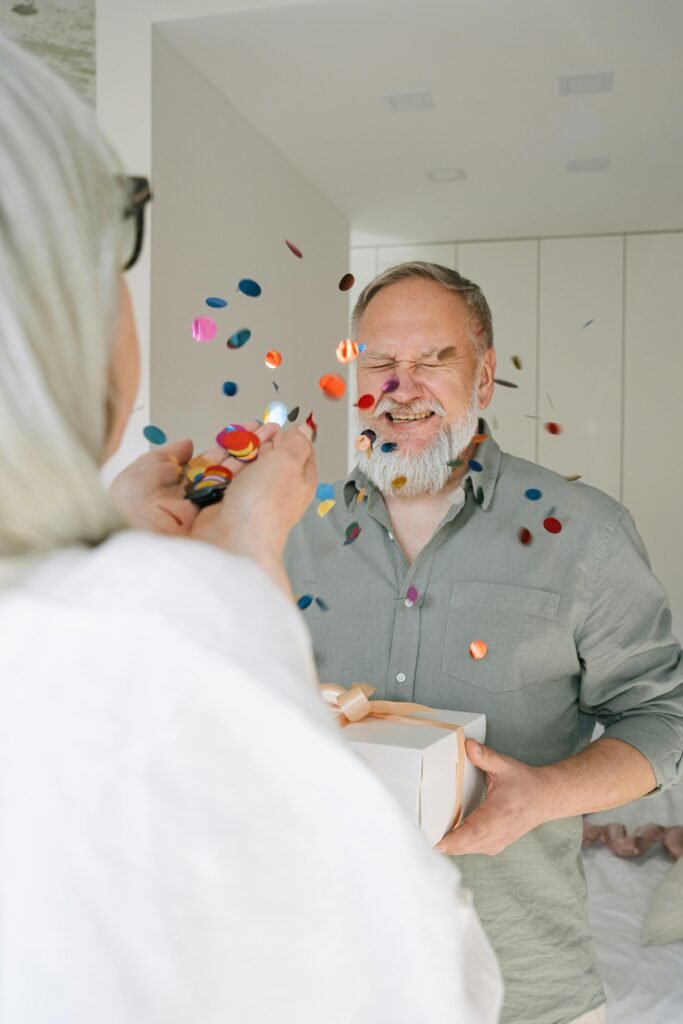 Joyful senior couple celebrating together with confetti indoors.